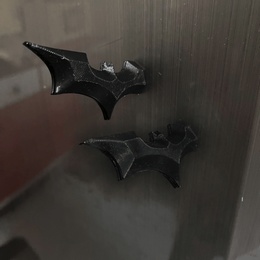 Pair of black Batarang-shaped fridge magnets attached to a metal refrigerator door.