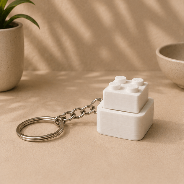 White 3D-printed Lego-brick-style fidget keychain with its top block raised up, angled view.