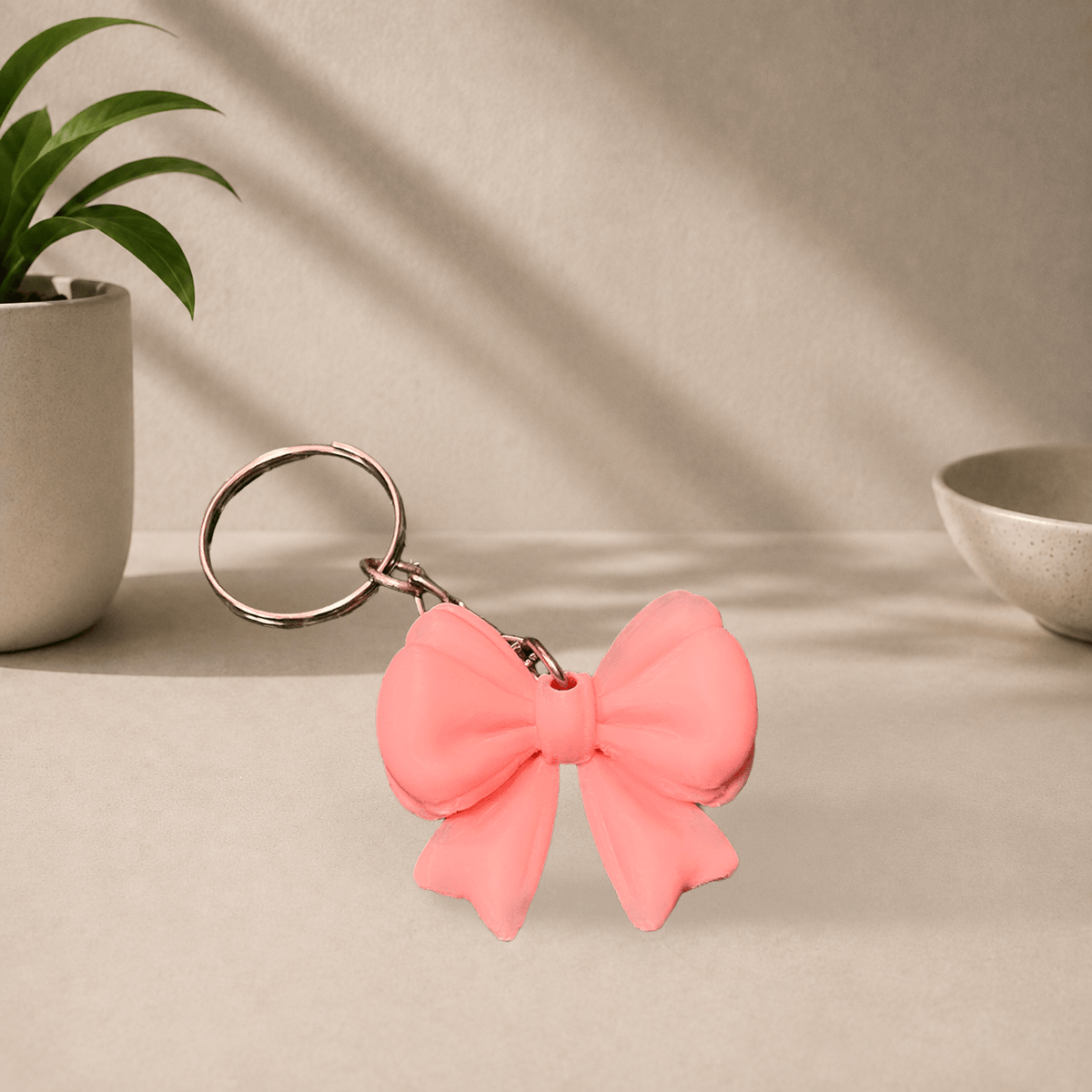 Light pink 3D-printed ribbon bow keychain hanging from a metal keyring.