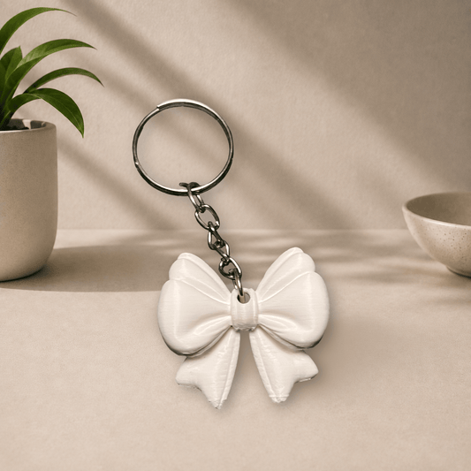 White 3D-printed ribbon bow keychain hanging from a metal keyring.