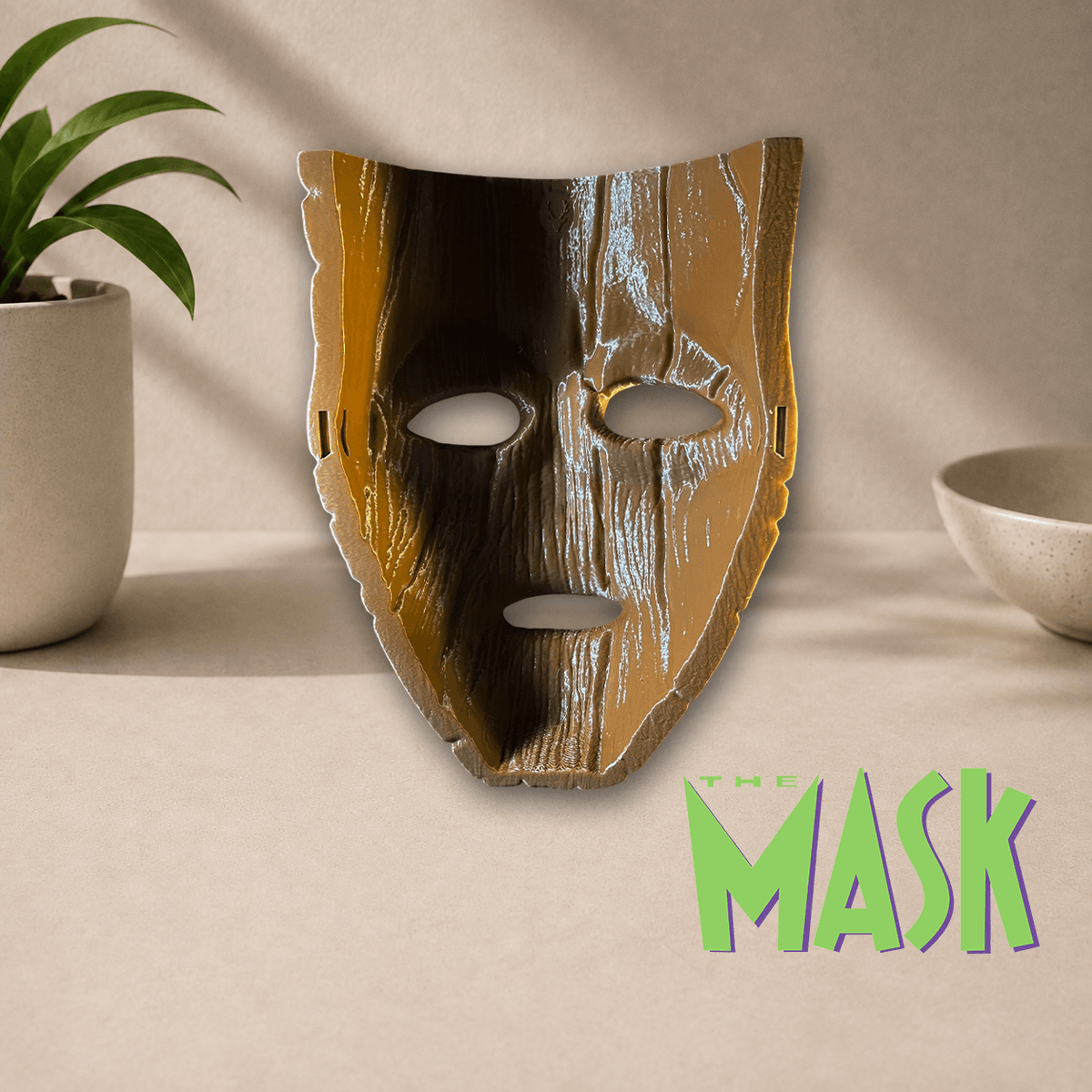 3D-printed 'The Mask' cosplay display mask in a glossy metallic gold and black finish, shown beside The Mask movie logo.