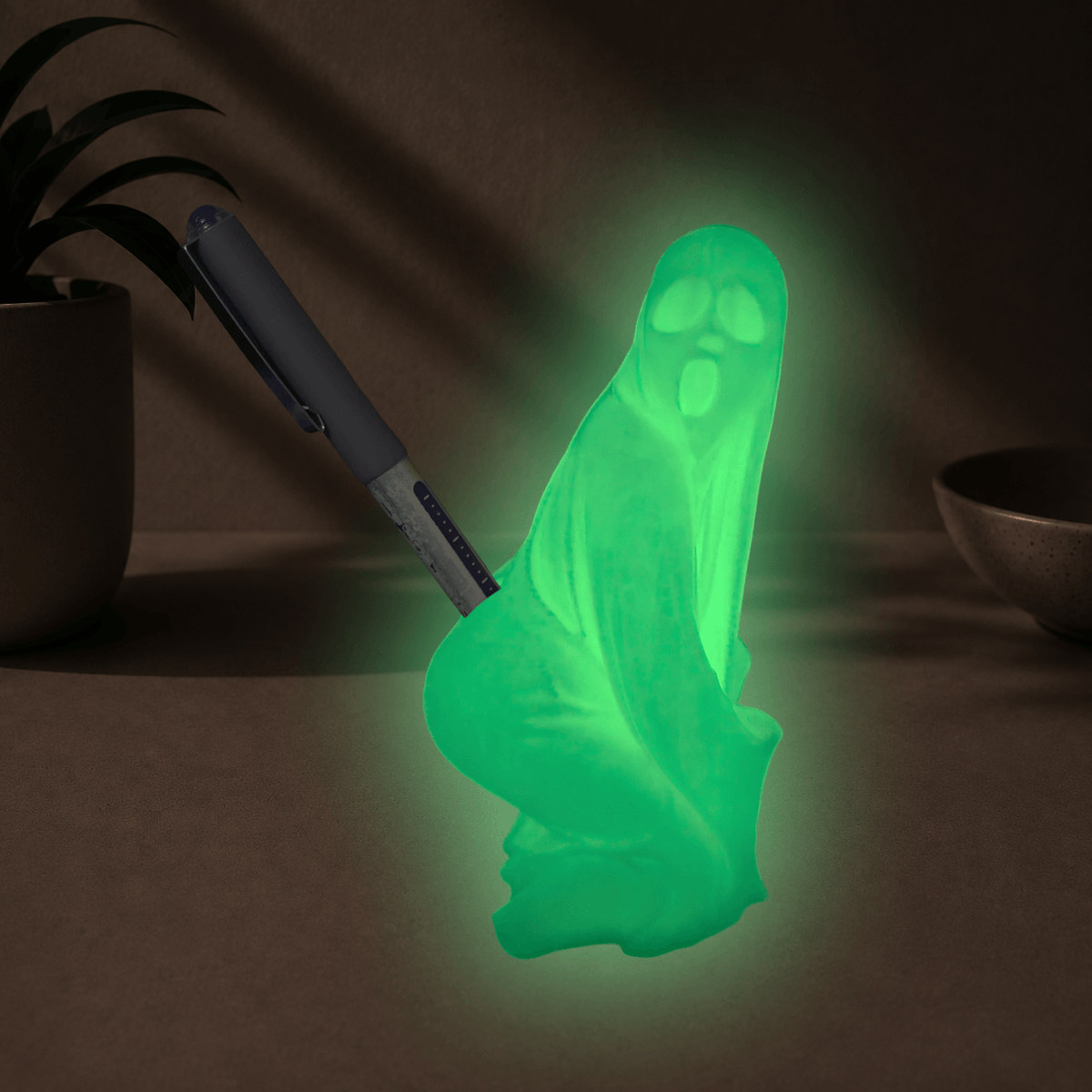 Glow-in-the-dark green twerking ghost pen holder glowing in a dark room, holding a pen