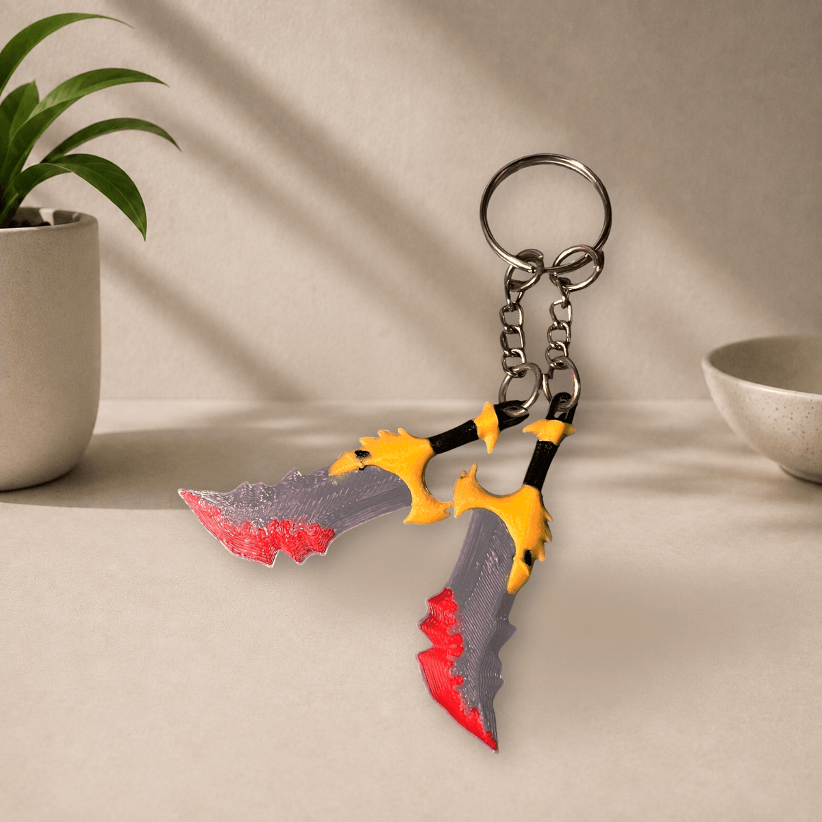 Pair of 3D-printed Blades of Chaos keychain charms (God of War) with red blood detailing painted on the tips, hanging from a metal keyring.