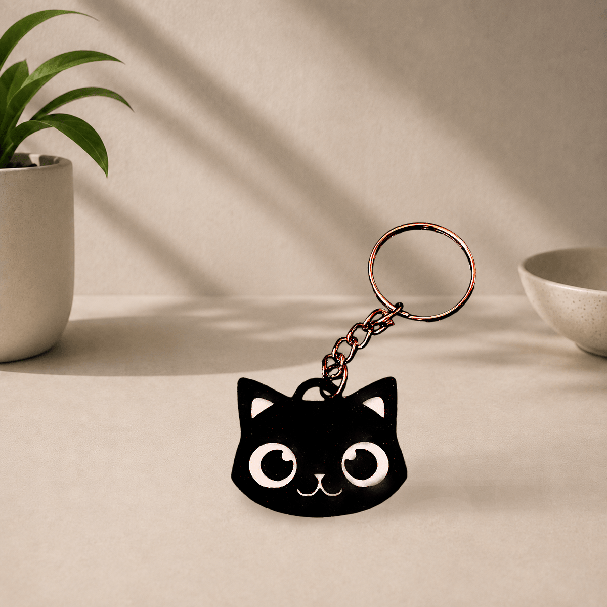 Black 3D-printed cat face keychain with white eyes, ears, and whiskers, hanging from a metal keyring.