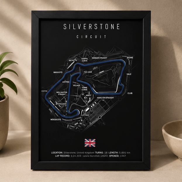 Black-framed 3D-printed Silverstone Circuit F1 track print with a blue highlighted route, standing upright on a table beside potted plants.