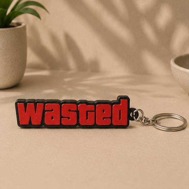 Red and black 'WASTED' text keychain inspired by GTA V, shown front-on on a beige tabletop.