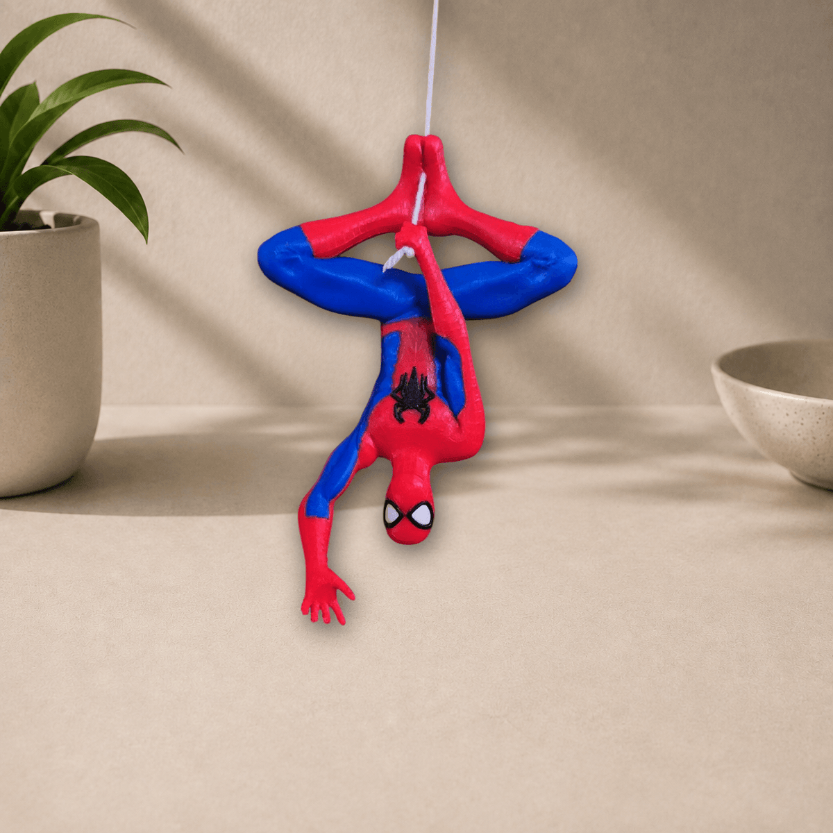 Red and blue 3D-printed hanging Spider-Man wall decor figure in an upside-down web-slinging pose, front view against a beige backdrop.