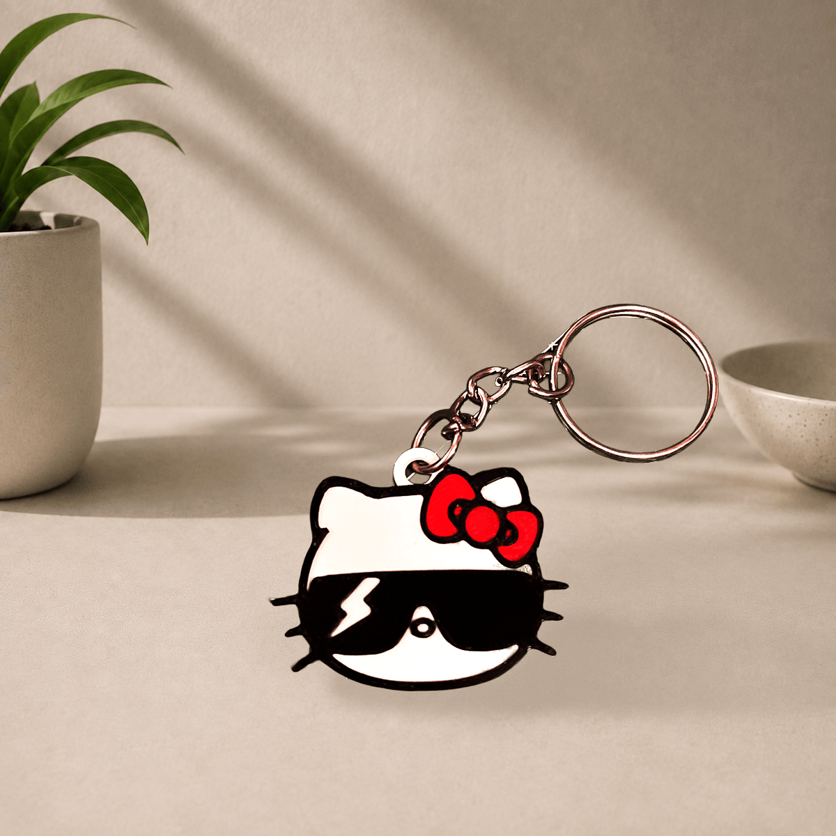 3D-printed Hello Kitty keychain wearing black sunglasses and a red bow, hanging from a metal keyring.