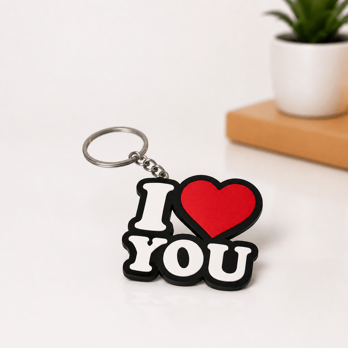 Close-up of a black 'I' and 'YOU' text-shaped keychain with a red heart in place of the word 'love,' hanging from a metal keyring.