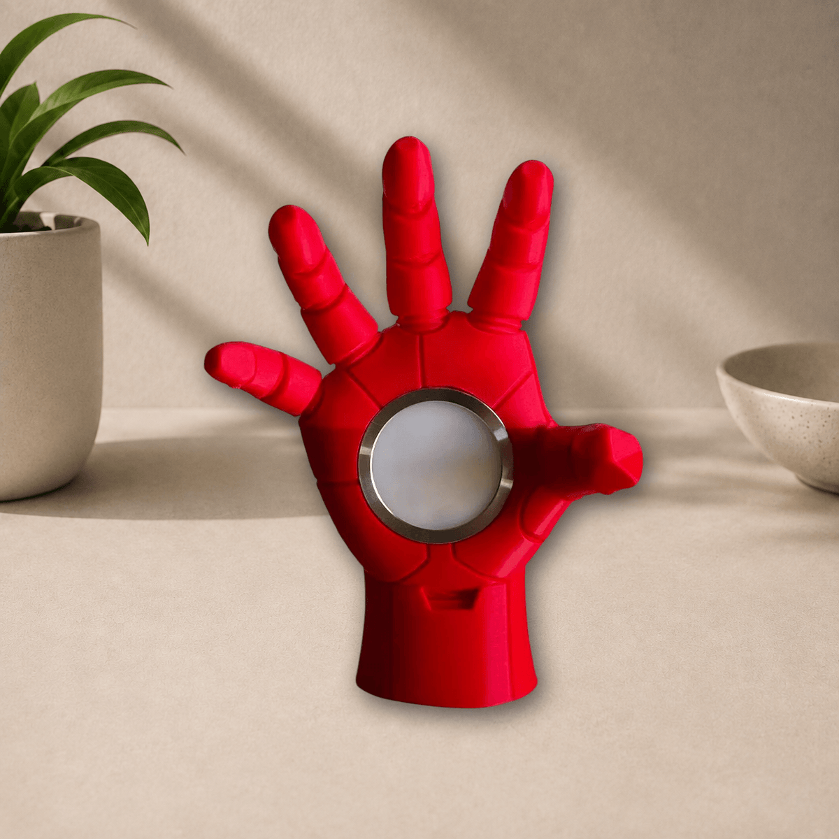 Red 3D-printed Iron Man hand-shaped lamp with an open palm and a round chest-arc-style light in the center, unlit, on a beige tabletop.