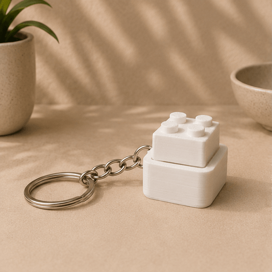 White 3D-printed Lego-brick-style fidget keychain with its top block raised up, angled view.