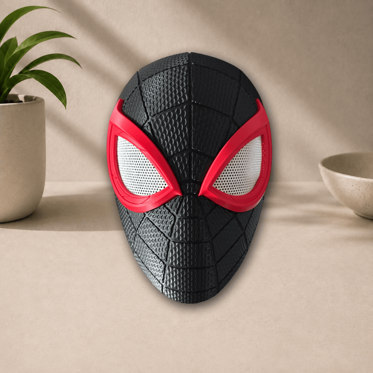 Black 3D-printed Miles Morales PS5 cosplay mask with red webbing lines and red-rimmed eye lenses, front view on a beige tabletop.