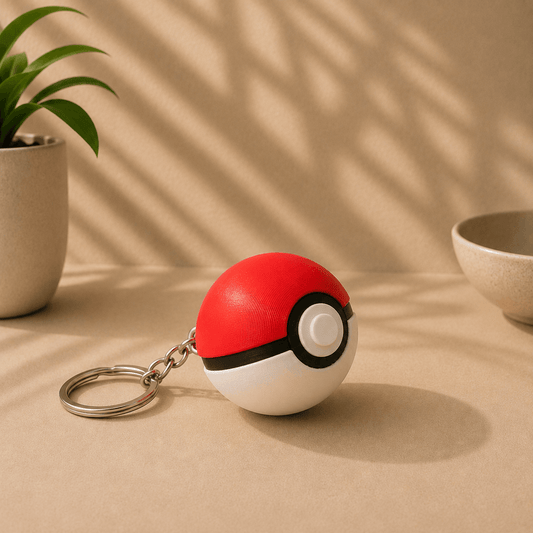 Pokeball-shaped fidget keychain on a metal keyring, displayed on a tabletop with a potted plant and ceramic bowl in the background.