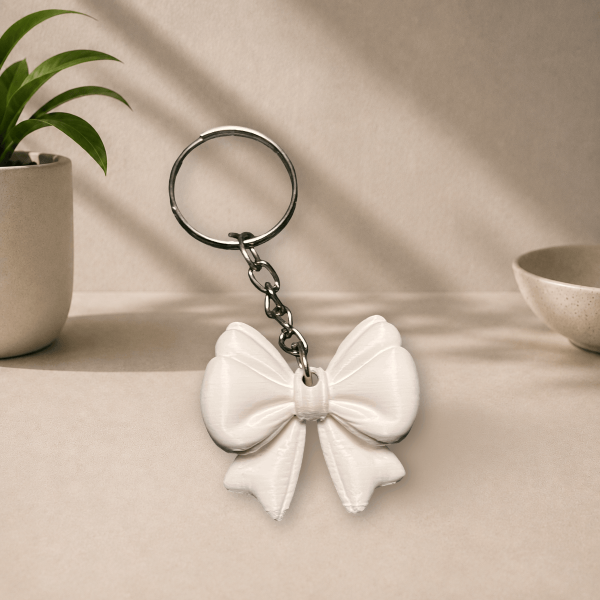 White 3D-printed ribbon bow keychain hanging from a metal keyring.