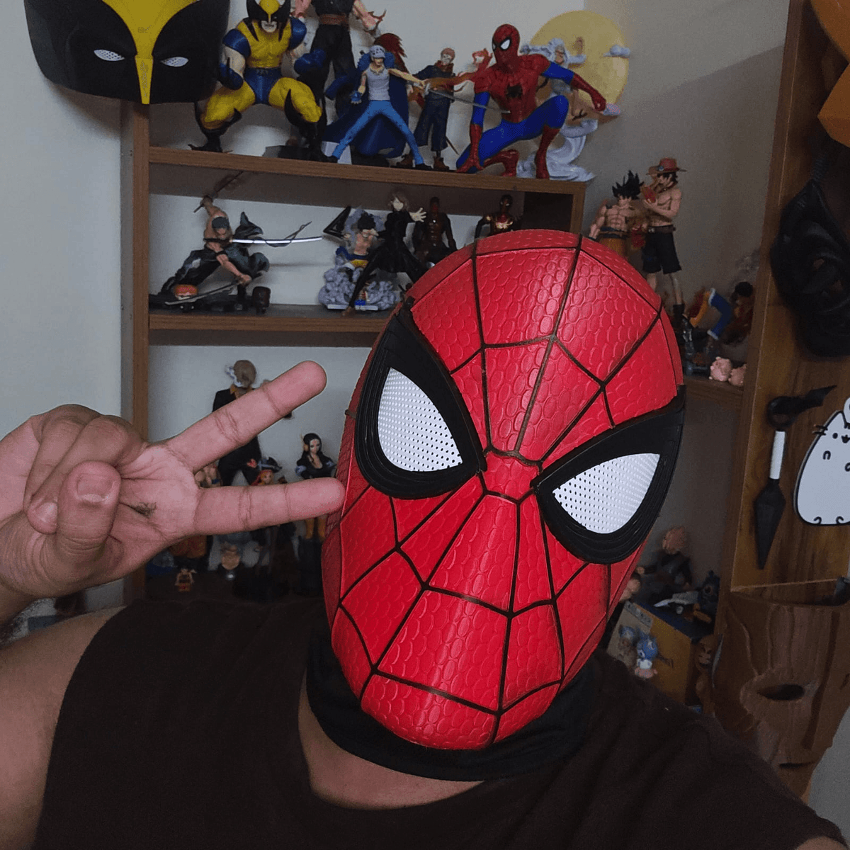 Person wearing the red 3D-printed Spider-Man Brand New Day cosplay mask, giving a peace sign in front of a shelf of collectible figures.
