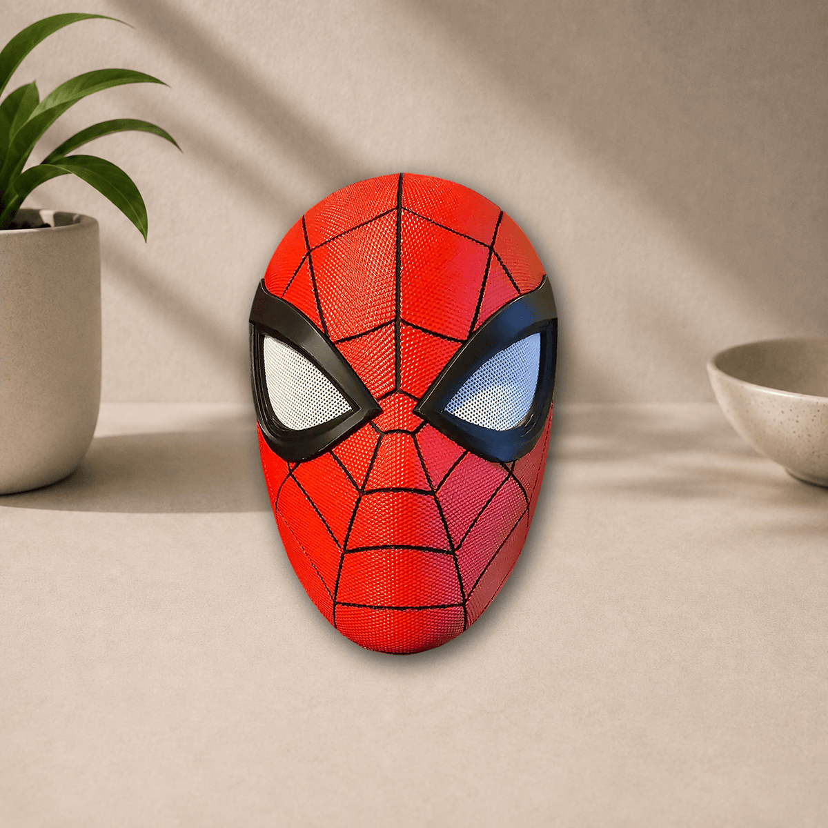 Red 3D-printed Spider-Man PS5 cosplay mask with black webbing lines and reflective eye lenses, front view on a beige tabletop.