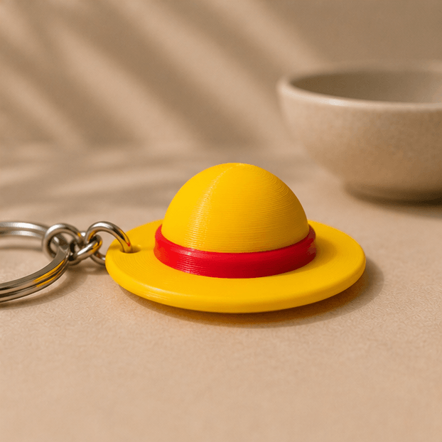 Close-up of the yellow straw hat charm from the One Piece Straw Hat Keychain, showing its red hatband.