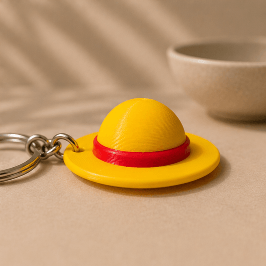 Close-up of the yellow straw hat charm from the One Piece Straw Hat Keychain, showing its red hatband.