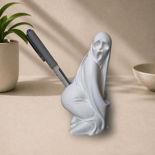 White 3D-printed twerking ghost pen holder holding a pen, desk decor with plant in background