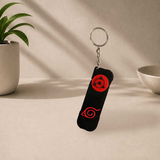 3D-printed Uchiha clan phone stand keychain from Naruto, folded flat showing the red Sharingan and Konoha leaf emblems, on a metal keyring.