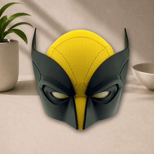 Black and yellow 3D-printed Wolverine cosplay mask with pointed ear fins, front view on a beige tabletop.