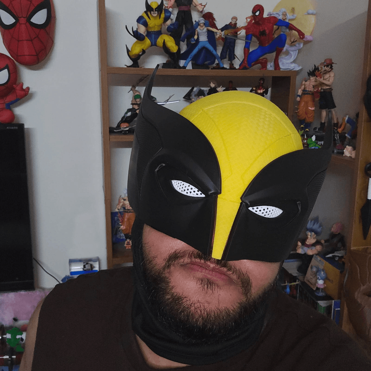 Person wearing the black and yellow 3D-printed Wolverine cosplay mask in front of a shelf of collectible figures.